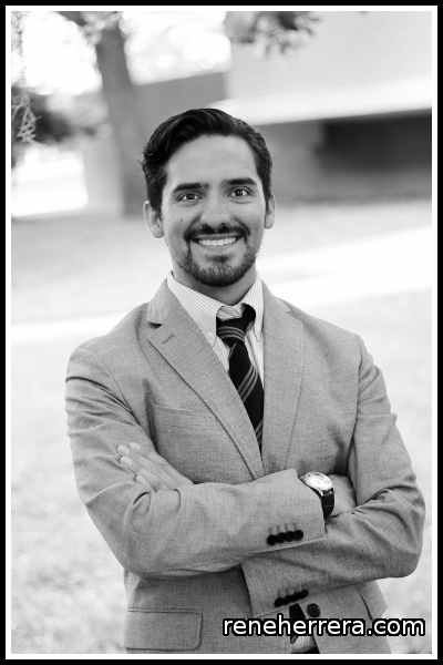 Black and white photo of a man wearing a suit and tie. The man is smiling and looking directly at the camera.